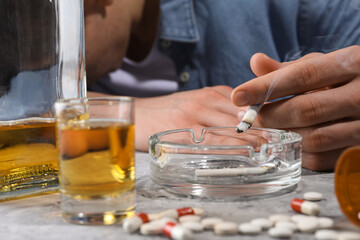 Alcohol and drug addiction. Man with smoldering cigarettes, whiskey and pills at grey table, selective focus