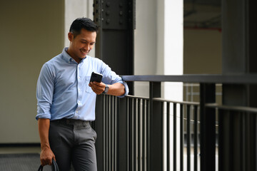 Handsome businessman with briefcase using smartphone at the walkway inside a building