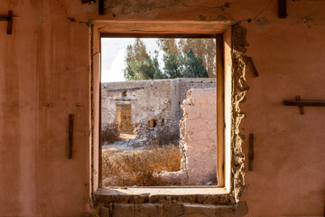 View through a broken window of ruined buildings and courtyard in Al Jazirah Al Hamra haunted town...