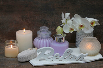 Spa composition with massage oil, orchid flower candles and the word Relax.	