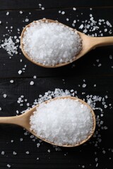 Organic salt in spoons on black wooden table, top view