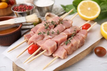 Skewers with cut raw meat, thyme and tomatoes on light table, closeup