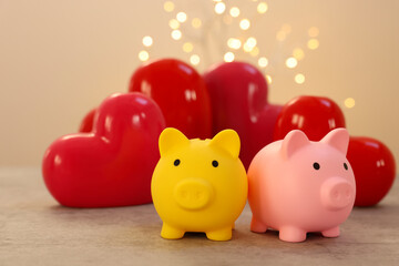 Piggy banks and ceramic hearts on grey table against blurred lights