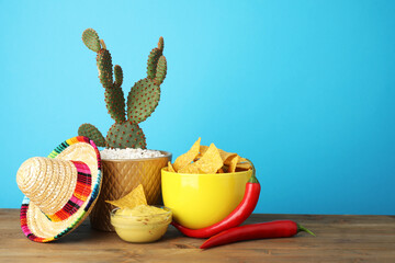 Mexican sombrero hat, cactus, chili peppers, nachos chips and guacamole in bowls on wooden table...