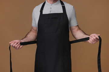 Man wearing kitchen apron on brown background, closeup. Mockup for design - obrazy, fototapety, plakaty