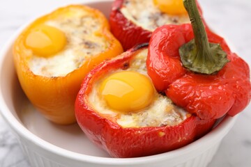 Delicious stuffed peppers with eggs in bowl on white table, closeup