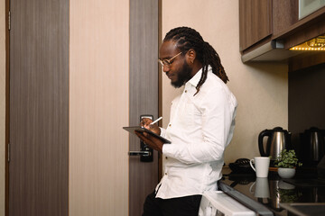 Happy millennial African man using digital tablet at kitchen counter