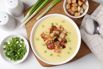 Tasty potato soup with bacon, green onion and croutons in bowl served on white table, flat lay
