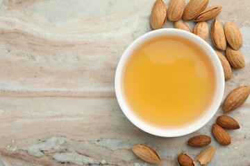 Almond oil in bowl and nuts on color marble table, flat lay. Space for text