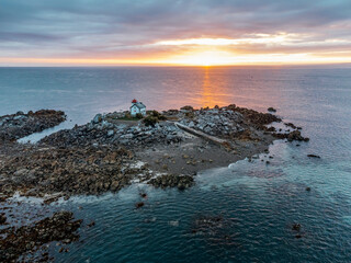 Sunrise in Harbour is a small rocky islet flanked by a narrow red-and-white lighthouse house, 1.8...