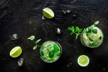 Mojito cocktail. Summer cold drink with lime, fresh mint, and ice. Cool beverage on a black slate background, shot from the top
