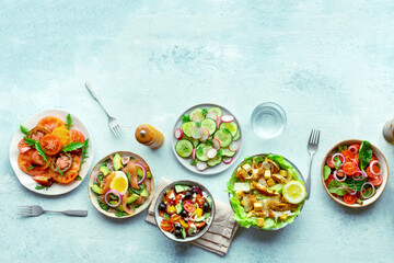Fresh salads, overhead flat lay shot of an assortment. Variety of plates and bowls with green...