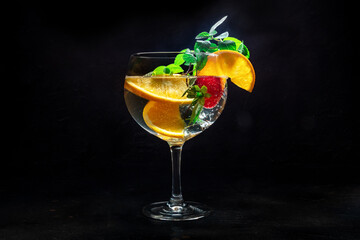 Fancy cocktail with fresh fruit. Gin and tonic drink with ice at a party, on a black background. Alcohol with orange, mint, and strawberry