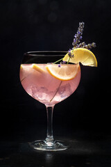 Cocktail with fresh fruit and flowers. Gin and tonic drink with ice at a party, on a black background. Alcohol with lavender and lemon