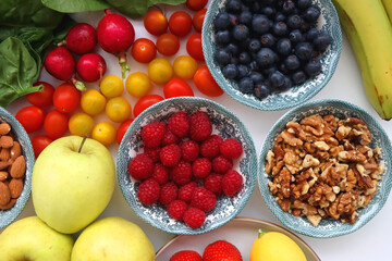 Apples, lemons, bananas, berries, carrots, leek, tomatoes, radishes, spinach and various nuts on white background. Healthy seasonal fruit and vegetable. Top view.
