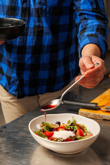 preparation of an exotic salad. Strawberry salad with herbs and stracciatella. Close-up. A chef's hand holds a spoon with strawberry syrup. Berry salad with cheese. Healthy food, light meals.