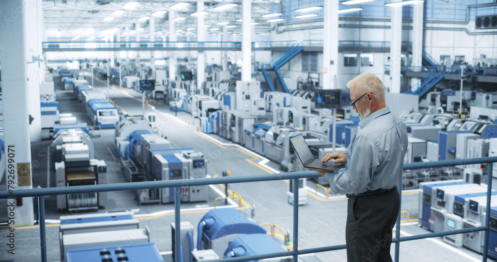 Poster Experienced Male Engineer Standing on a Platform, Using Laptop Computer and Overlooking Production at a Modern Automated Electronics Manufacture with AI Support. Factory Executive at Work