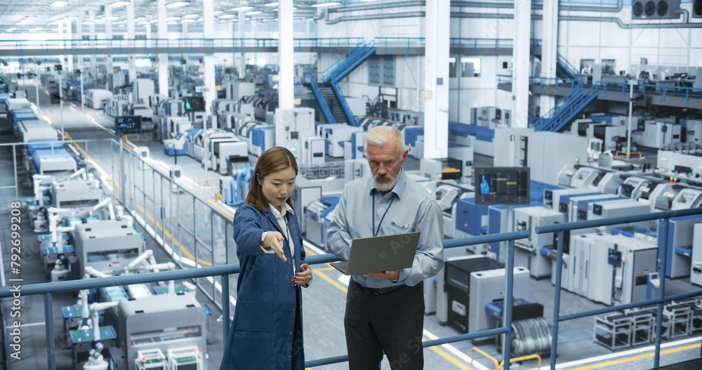 Poster portrait of a middle aged engineer and happy asian scientist using laptop computer and talking in a 