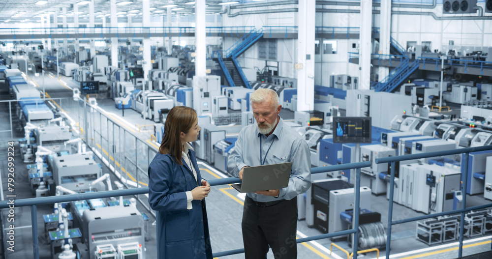Poster Male Engineer and Female Project Manager Standing on a Platform, Talking, Using Laptop Computer and Monitoring Production at a Modern Automated Electronics Manufacture with AI Robots