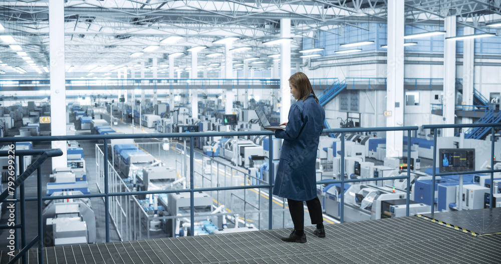 Leinwandbilder Thoughtful Asian Engineer Monitoring and Analyzing Conditions at a Pristine Modern Electronics Factory with Automated Robot Hands Working with the Help of Artificial Intelligence Software