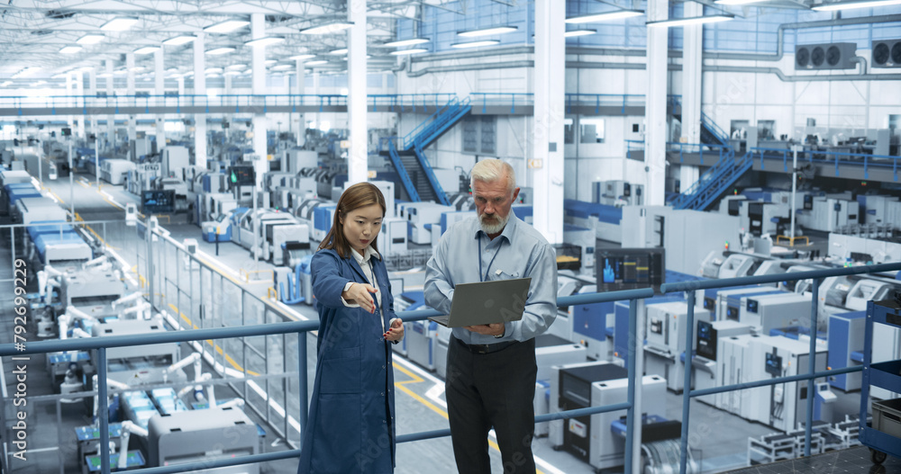 Poster Middle Aged Engineer and Young Japanese Technician Having a Conversation and Using Laptop Computer. Specialists Monitoring, Analyzing Conditions at a Modern Electronics Factory with Automated Robots
