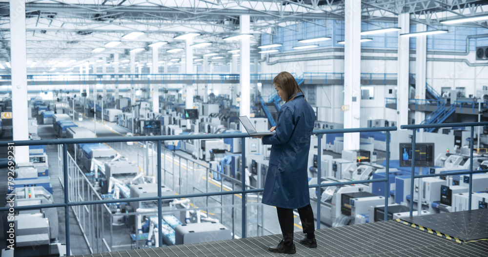 Poster Experienced Female Engineer Standing on a Platform, Using Laptop Computer and Overlooking Production at a Modern Automated Electronics Manufacture with AI Support. Factory Manager at Work
