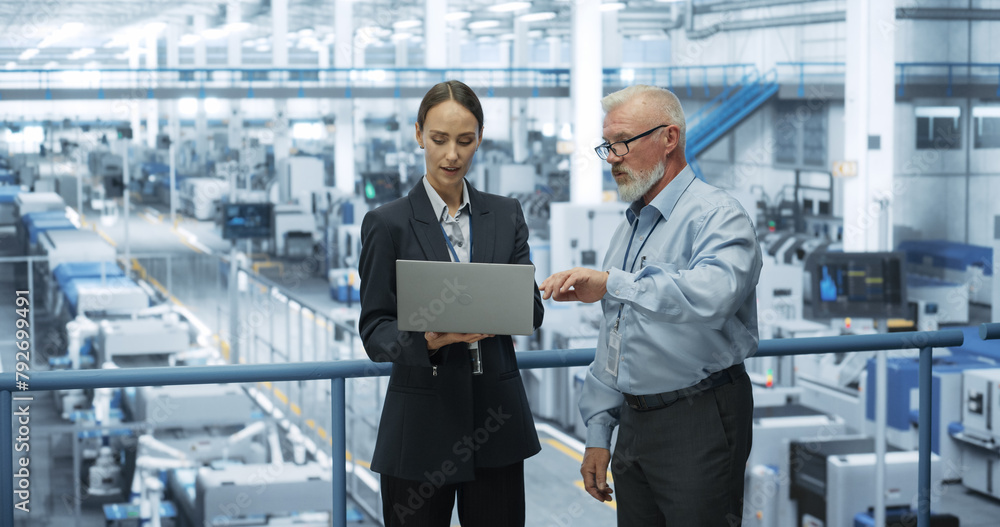 Aufkleber Experienced Male and Female Engineers Standing on a Platform at a Modern Industrial Factory, Using Laptop Computer and Discussing Production of Modern Electronics for Artificial Intelligence Machines