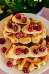 Viennese waffles with raspberries and bananas on a white plate next to yellow flowers in a pot. plain light background. homemade baking. recipe