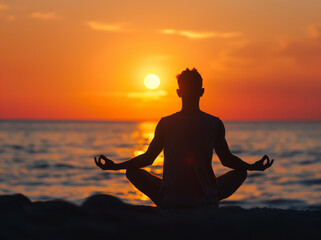 Silhouette of man meditating in lotus position against sunset sky background, doin yoga for relaxation and health on beach at sunrise.