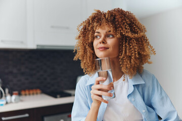 Attractive African American woman with glass of water standing in modern kitchen at home, healthy...