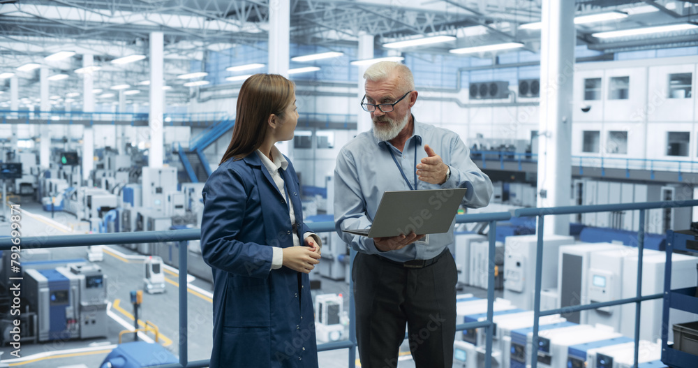 Aufkleber Two Diverse Engineers Standing on a Platform, Using Laptop Computer at an Electronics Factory. Machines are Producing Electronic Chips, Specialists Monitoring the Progress on Online Software