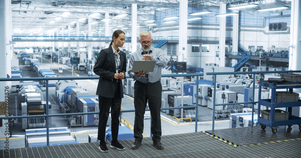 Aufkleber Middle Aged Engineer and Young Female Technician Having a Conversation and Using Laptop Computer. Specialists Monitoring, Analyzing System Reports at a Modern Electronics Factory
