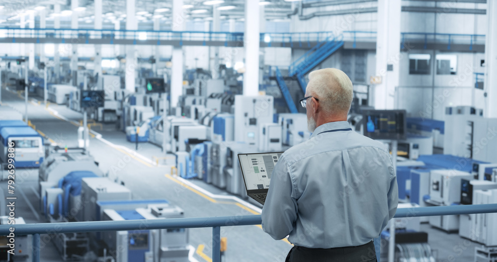 Poster Portrait of an Adult Engineer Standing on a Platform, Using Laptop Computer at an Electronics Factory. Technician Making Technical Upgrades Online Over an Internet Software