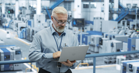 Middle Aged Engineer Monitoring and Analyzing Conditions at an Automated Modern Electronics Factory with Mobility Robots Working with the Help of Artificial Intelligence Software - 792699899