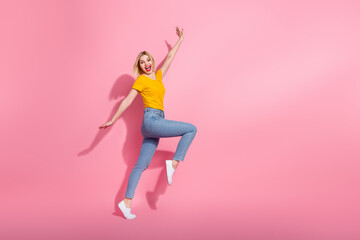 Full length photo of cute positive woman wear yellow t-shirt jumping high empty space isolated pink...