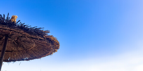 Edge of a straw beach umbrella against a blue sky background with large copy space. Summer holiday...