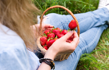 Young woman eats ripe strawberries sitting on the grass. Healthy lifestyle concept. Selective focus.