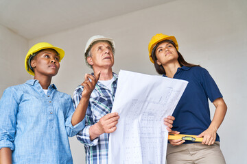 Female construction workers discussing over blueprint design with senior male contractor at...