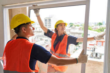 Female and male carpenters wearing safety workwear installing window frame in house construction...