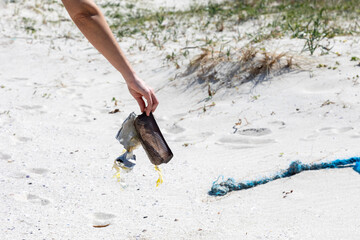 A conscious female helps clean the beach by picking up a blue piece of trash on a sunny day,...