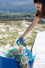 A conscious female helps clean the beach by picking up a blue piece of trash on a sunny day,...