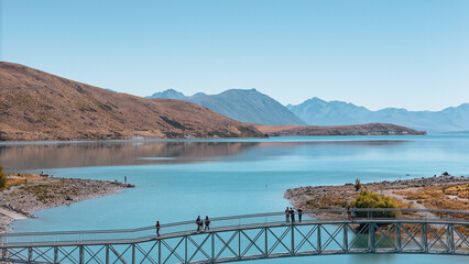 View of Lake Tekapo, mountains, and people on a bridge sightseeing in New Zealand