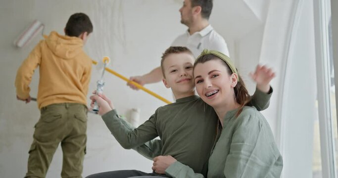 A family of four, including two young boys and their parents, painting the walls of their new home.Teamwork of a family doing DIY renovations, conveying a sense of collaboration and new beginnings.