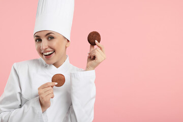 Happy professional confectioner in uniform holding delicious macarons on pink background. Space for...