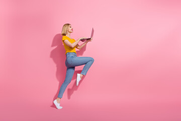 Full length photo of cute excited lady dressed yellow t-shirt jumping typing emails device empty space isolated pink color background
