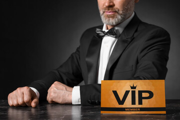 Man sitting at table with VIP sign on black background, closeup