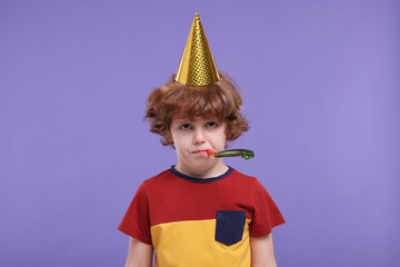 Sad little boy in party hat with blower on purple background