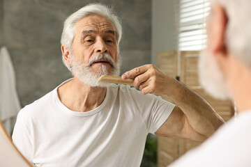 Senior man with mustache combing beard near mirror in bathroom