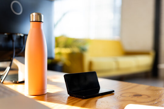 A pink water bottle and black wallet resting on wooden table in a modern office, copy space