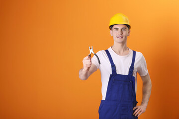 Young man holding pliers on orange background, space for text